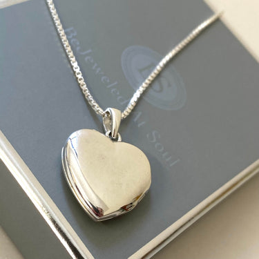 Heart-shaped silver locket on a chain against a gray background