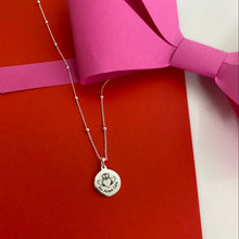 Silver necklace with a pendant on a red surface with pink paper