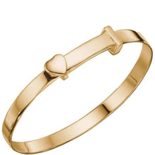 A polished gold-plated bangle bracelet with a small heart-shaped charm on a plain white background.
