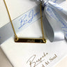Gold necklace with a nameplate on a branded box with a silver ribbon.