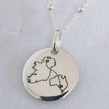A silver round disc pendant necklace with a hand-drawn outline of Ireland, displayed on a light gray jewelry box.