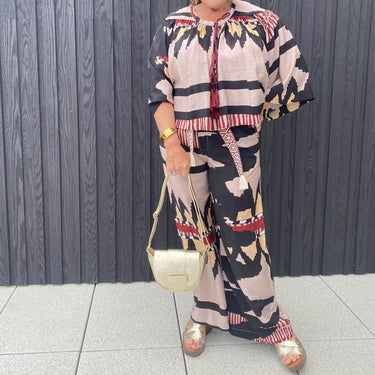 Person wearing a patterned outfit with a gold handbag against a wooden panel background