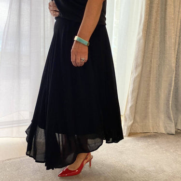 Person wearing a black dress with red shoes in a room with curtains.