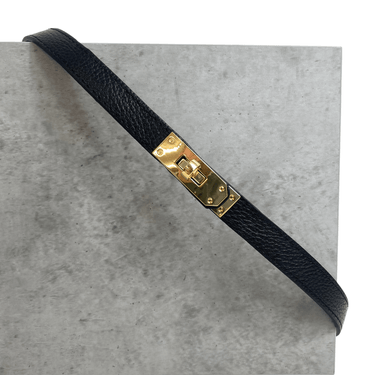 Black leather strap with a gold buckle on a gray surface