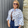 Woman wearing a polka dot blouse and sunglasses against a wooden and stone wall.