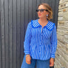 Woman wearing a blue and white striped shirt against a wooden and stone wall.