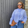 Woman wearing a blue striped shirt and sunglasses, standing against a wooden wall.