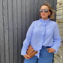 Woman wearing a blue striped shirt and sunglasses, standing against a wooden wall.
