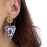 Heart-shaped earring with blue and white design worn by a person