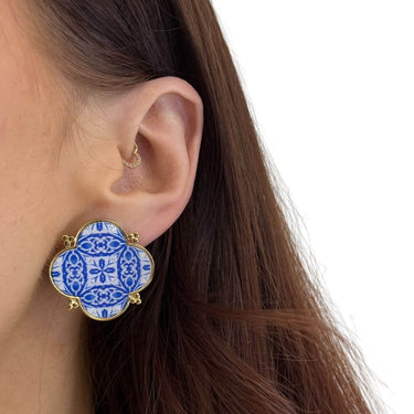 Close-up of an ear wearing a blue and white patterned earring with gold accents.