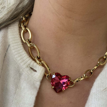 Gold chain necklace with a red heart pendant worn by a person in a white cardigan.