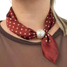Red polka dot scarf with a pearl knot around a person's neck, wearing a brown top.