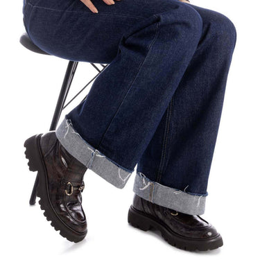 Person wearing blue jeans and brown boots sitting on a chair with a white background