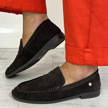 brown suede penny loafers worn with bright red trousers on a light gray wood floor.