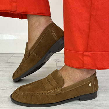 A person wearing brown suede penny loafers and bright red cropped pants, standing on a light gray wood floor.