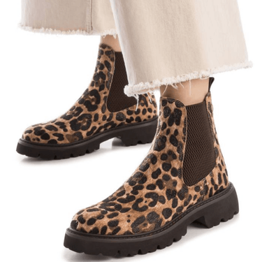 Leopard print Chelsea boots worn with light-colored pants on a white background