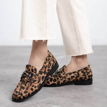 Leopard print loafers worn with white pants on a neutral background