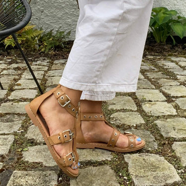 Person wearing white pants and brown sandals on a stone path with plants in the background