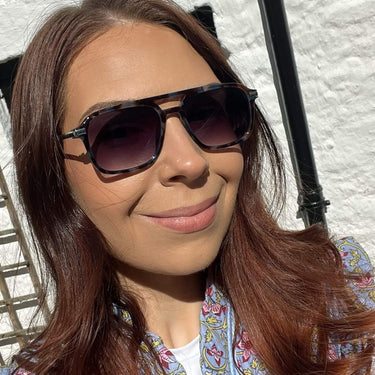 Woman wearing sunglasses with a white textured wall background