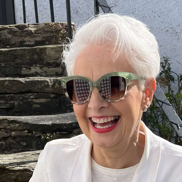 Woman wearing sunglasses and a white jacket with a red skirt standing on stone steps.