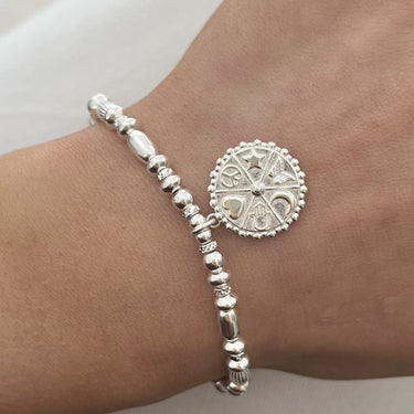 Silver bracelet with a round decorative element on a wrist against a neutral background
