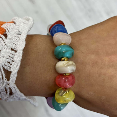 Colorful beaded bracelet on a wrist with a white lace sleeve against a white background