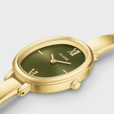 A close-up of a Cluse watch featuring a polished gold-tone case and strap, with an olive green dial and gold-tone Roman numeral hour markers, set against a light gray background.