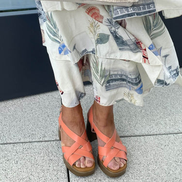 Person wearing coral sandals and floral pants on a concrete surface