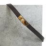 Brown leather belt with a gold buckle on a gray concrete surface
