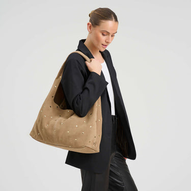 Woman holding a beige tote bag with gold studs against a light gray background
