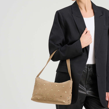 Woman holding a beige handbag against a plain background