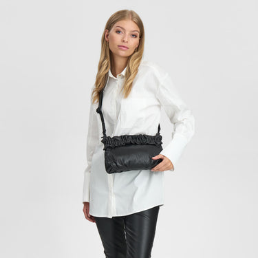 Woman wearing a white shirt and black leather pants with a black bag over her shoulder on a light gray background