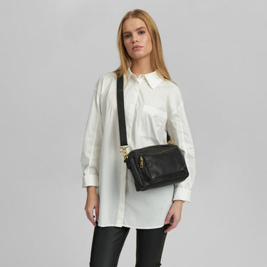 Woman wearing a white shirt and black leather bag on a gray background