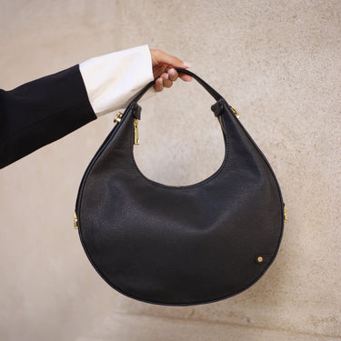 Black handbag held by a person against a neutral background