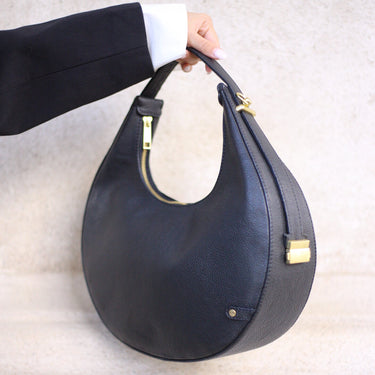 Black handbag with gold accents held by a person against a neutral background