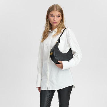 Woman holding a black handbag against a plain background