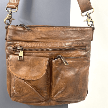 Brown leather handbag with gold zippers on a gray background
