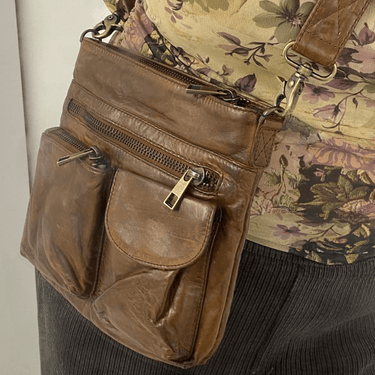 Brown leather bag with multiple zippers worn by a person in a floral top and dark pants.