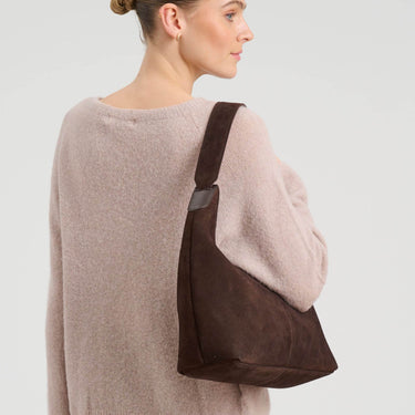 Woman wearing a brown leather shoulder bag on a plain background