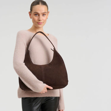 Woman holding a brown leather handbag against a light gray background