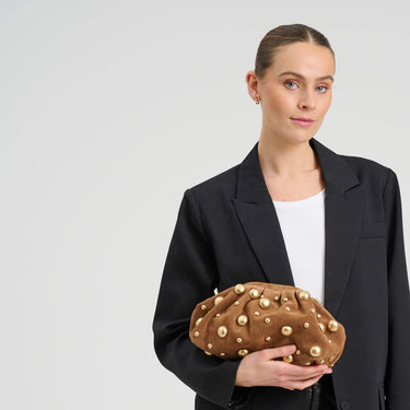 Woman holding a brown clutch with gold studs against a plain background