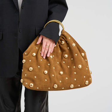 Brown handbag with gold studs held by a person wearing a black suit.