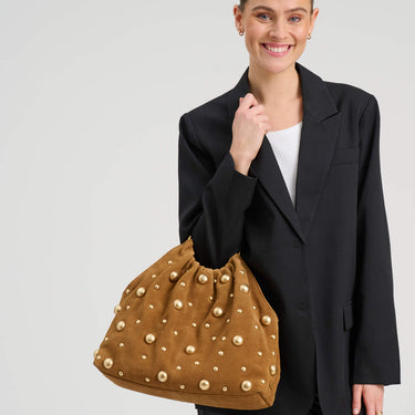 Woman holding a brown studded handbag against a plain background