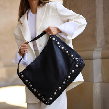 Person holding a black studded handbag against a neutral background