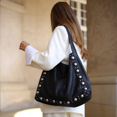 Woman carrying a black handbag with pearl-like embellishments in an indoor setting.