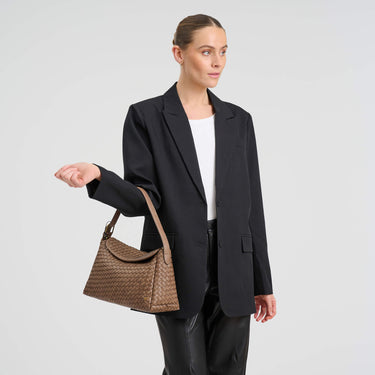 Woman holding a brown handbag wearing a black blazer on a light gray background