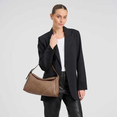 Woman holding a brown handbag against a plain background
