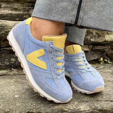 Blue sneakers with yellow accents worn on a stone surface