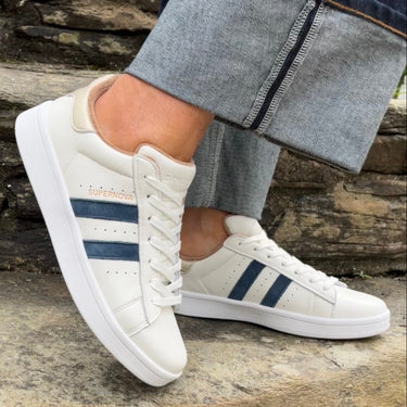 White sneakers with blue stripes worn by a person on a stone wall