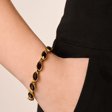Gold bracelet with dark beads on a wrist against a black background